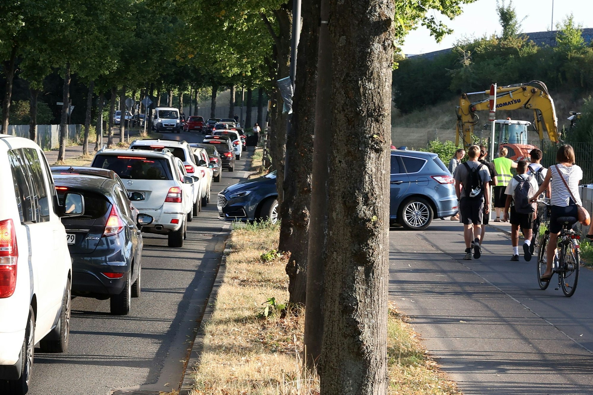 Autos reihen sich im dichten Verkehr an der Sürther Straße auf. Radfahrer und Fußgänger drängeln sich auf dem benachbarten Bürgersteig.