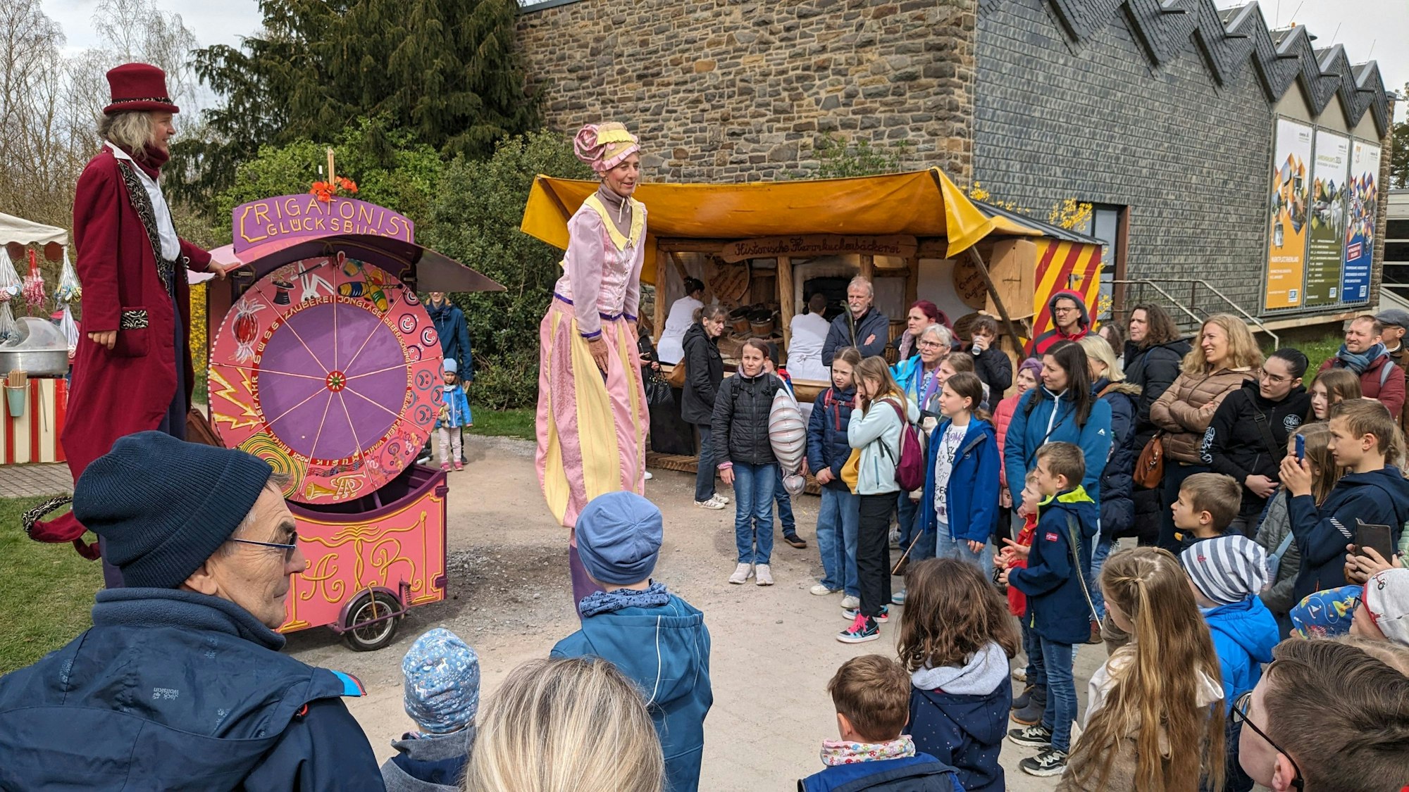 Das Publikum staunt über auf Stelzen gehende Akteure, die Betreiber eines Jahrmarkts aus früheren Jahrhunderten darstellen.