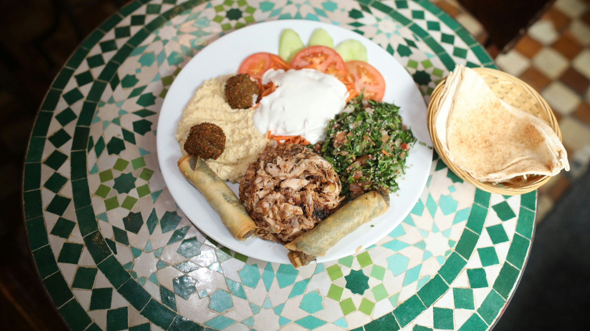 Schawarma, Gemüse, Humus, Blätterteigrollen und Brot sind auf einem Teller angerichtet.
