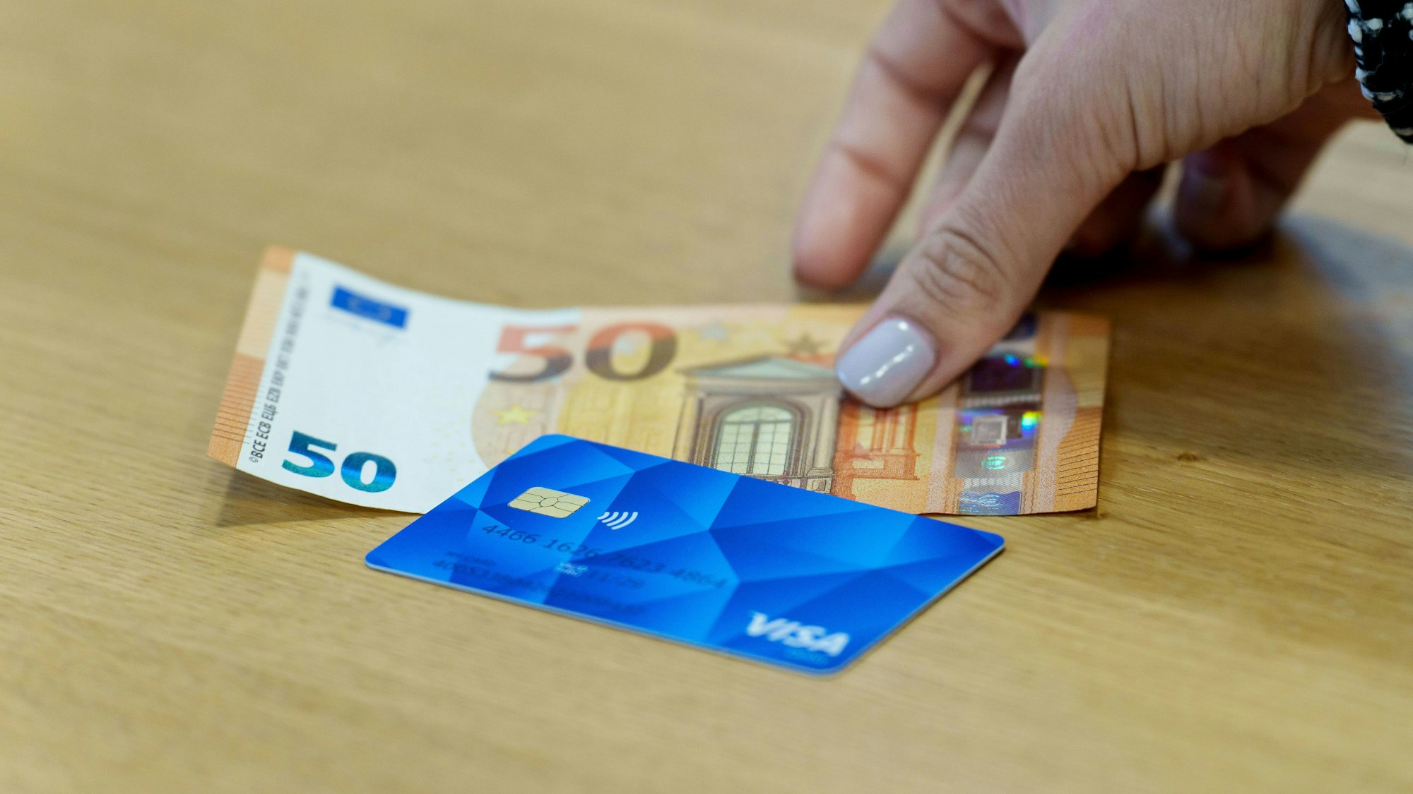 Die Bezahlkarte für Asylbewerberinnen und Asylbewerber und ein 50 Euro Schein liegen nebeneinander.